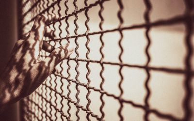 Hands on a wire-mesh prison enclosure to illustrate the article Is Purgatory Biblical?